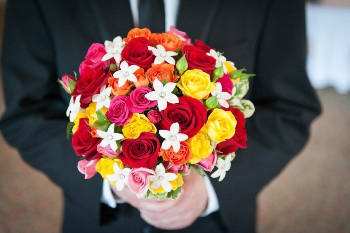 A man is holding a bouquet of colorful roses.