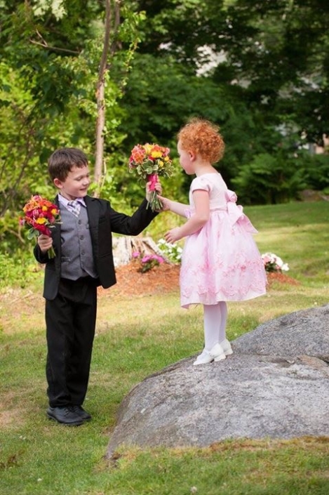 A boy and a girl holding flowers on a rock.