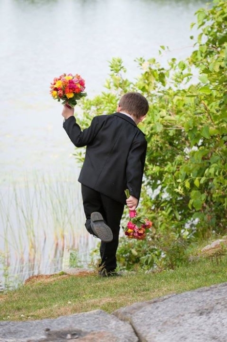 A boy in a tuxedo is running towards a body of water.