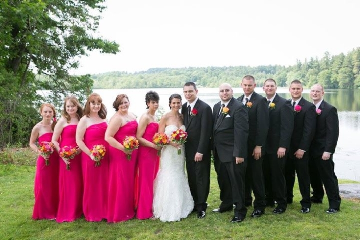 A group of bridesmaids and groomsmen standing in front of a lake.