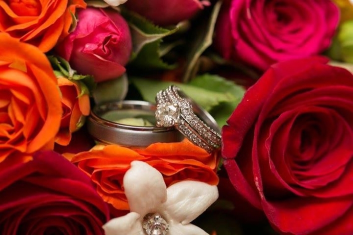 A wedding ring sits on a bouquet of orange and red roses.