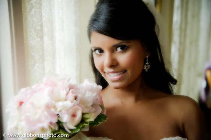 A bride holding a bouquet of pink flowers in front of a window.