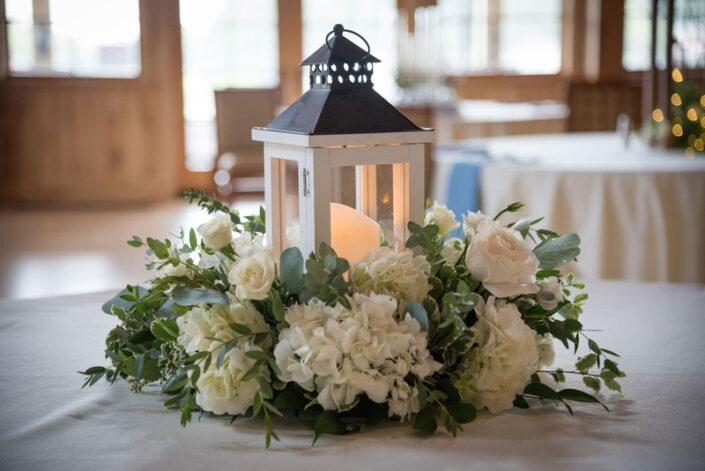 A lantern centerpiece with white flowers on a table.