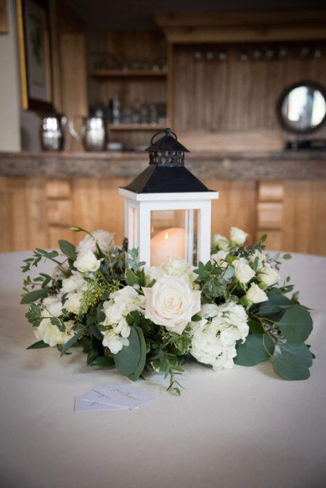 A lantern centerpiece with white flowers on a table.
