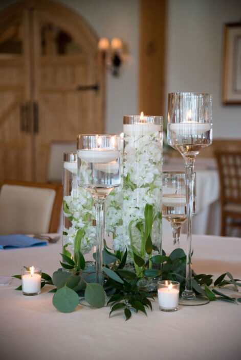 A centerpiece with candles and greenery on a table.