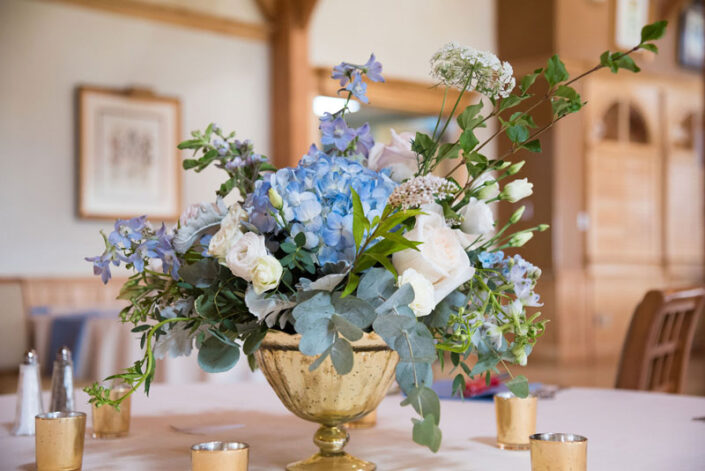 A gold vase with blue and white flowers on a table.