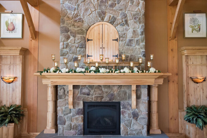 A stone fireplace is decorated with candles and flowers.
