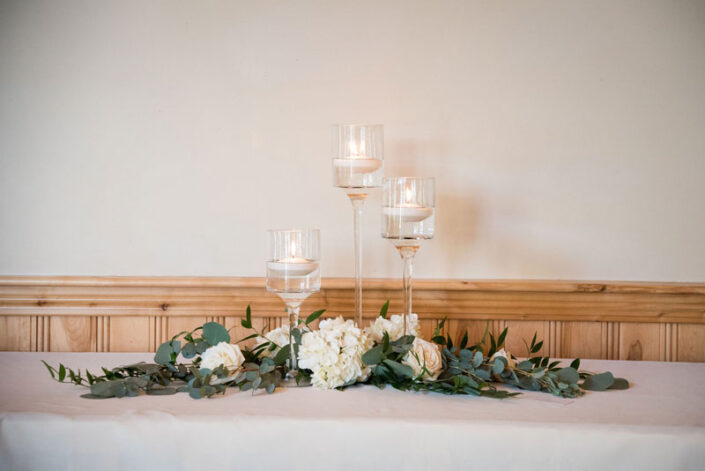 A table with candles and greenery on it.