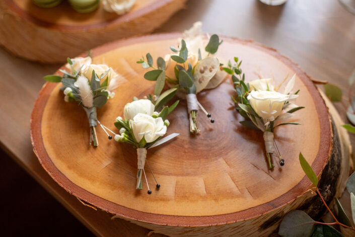 Four boutonnieres with white flowers on a wooden board.