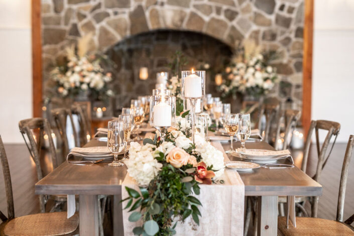 A table with candles and flowers in front of a stone fireplace.