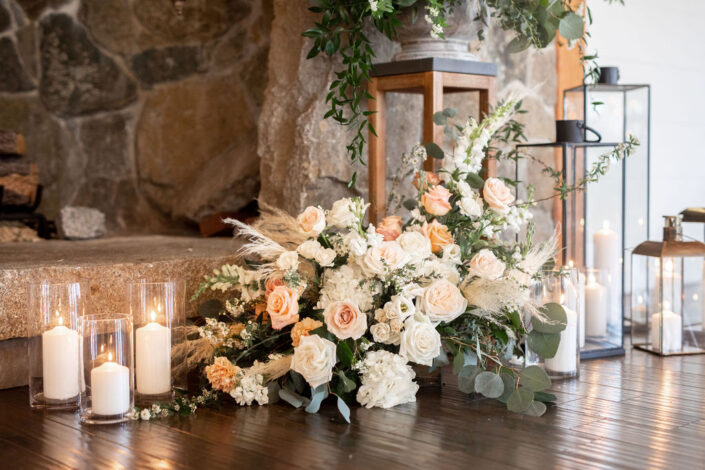A large arrangement of flowers and candles in front of a fireplace.
