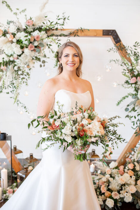 A bride in a white dress poses with her bouquet in front of a hexagonal backdrop.