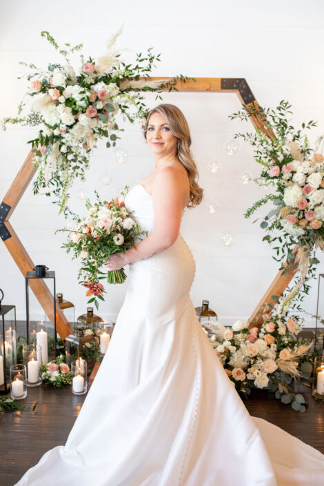 A bride in a white dress standing in front of a hexagonal wedding arch.