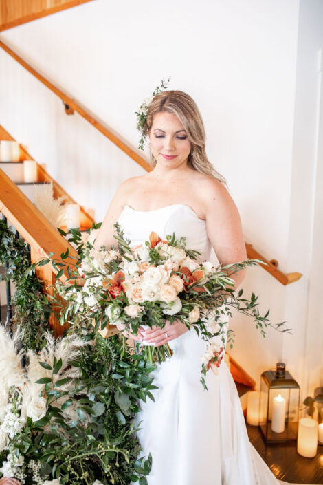A bride in a white dress standing on a staircase holding a bouquet.
