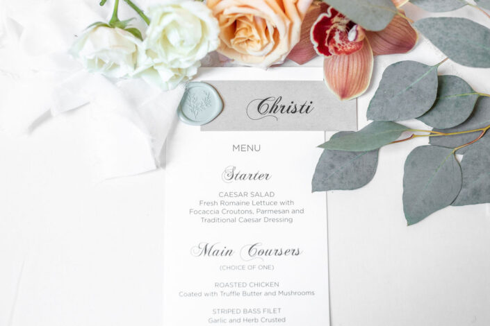A wedding menu with flowers and a wax seal.