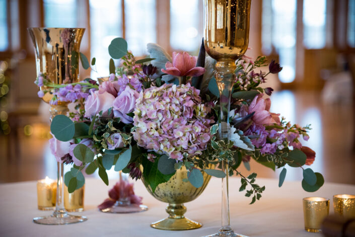 A gold vase filled with flowers and candles on a table.