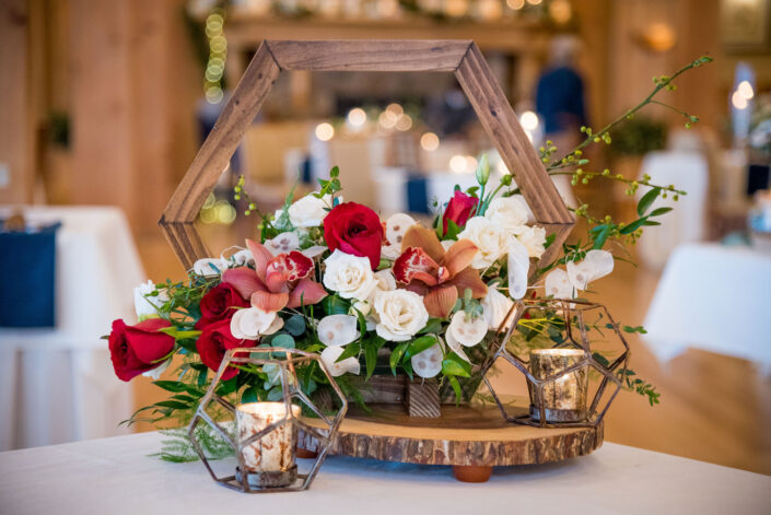 A centerpiece with red and white flowers on a wooden board.