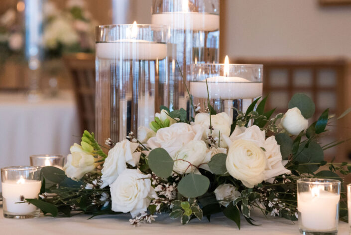 A centerpiece with white flowers and candles on a table.