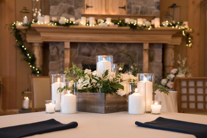 A table with candles and flowers in front of a fireplace.