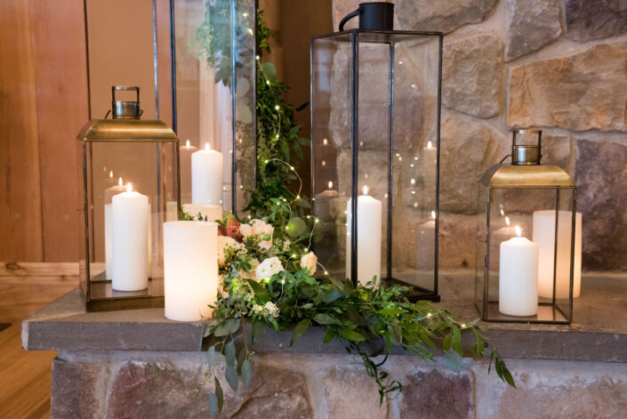 Three lanterns with candles and greenery on a stone wall.