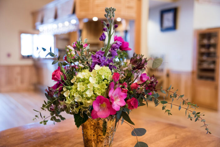 An arrangement of flowers in a gold vase on a wooden table.