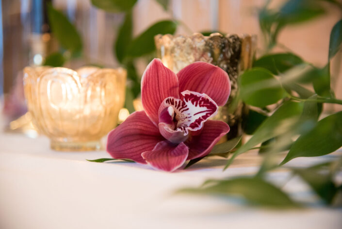 A burgundy orchid sits on a table next to a candle.
