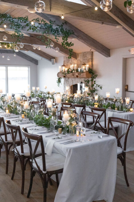 A wedding reception set up with white linens and greenery.