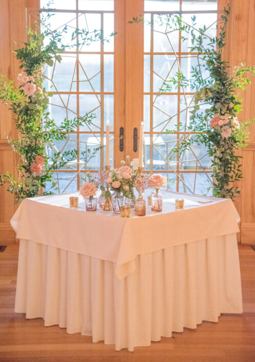 A table with flowers and greenery in front of a window.