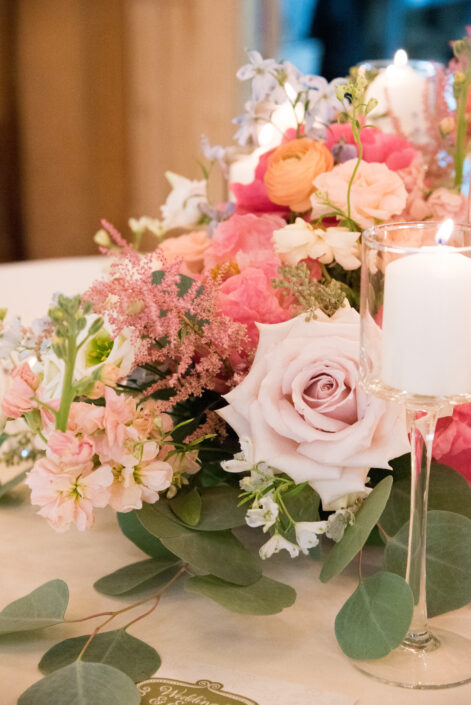 A pink and white centerpiece with candles and eucalyptus.