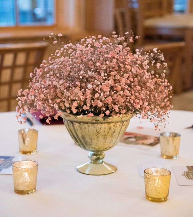 A gold vase with pink flowers and candles on a table.