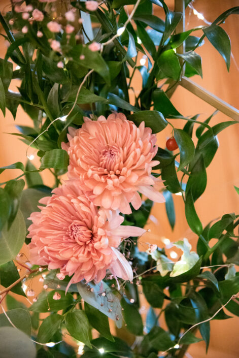 Pink chrysanthemums in a vase with green leaves.