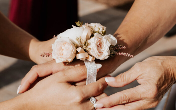 A woman is putting a flower corsage on a woman's hand.