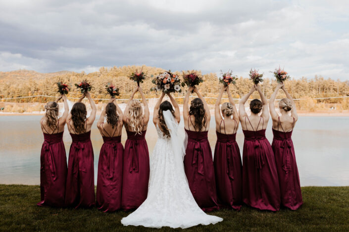 A group of bridesmaids in burgundy dresses standing in front of a lake.