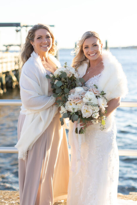Two bridesmaids posing for a photo by the water.