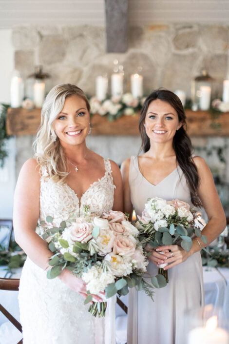 Two bridesmaids holding bouquets in front of a fireplace.