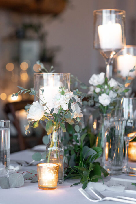 A white table setting with candles and greenery.