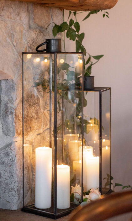 Two lanterns with candles on top of a stone fireplace.