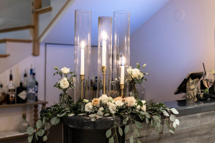 An arrangement of flowers and candles on a bar.