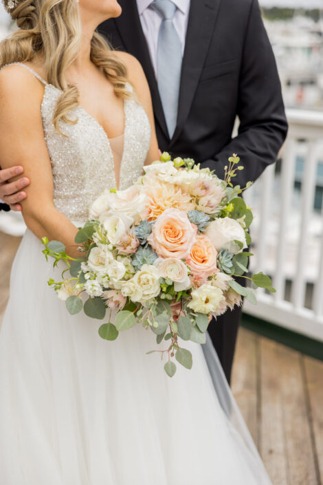 A bride and groom standing on a dock with their wedding bouquet.