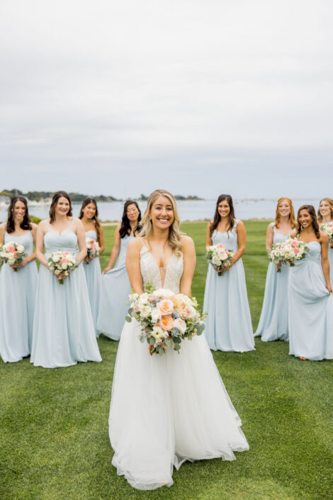 A bride and her bridesmaids in light blue dresses in front of the ocean.