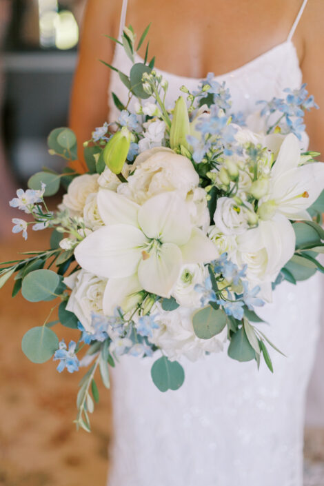 A bride holds a blue and white wedding bouquet.