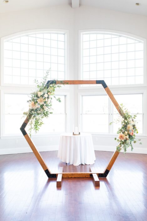 A hexagonal wedding arch made of wood and flowers.