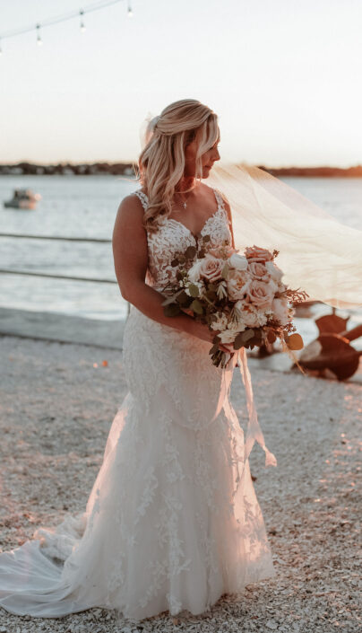 A bride holding her wedding bouquet on the beach at sunset.