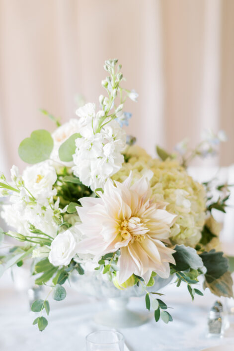 Dahlias and eucalyptus in a white vase on a table.