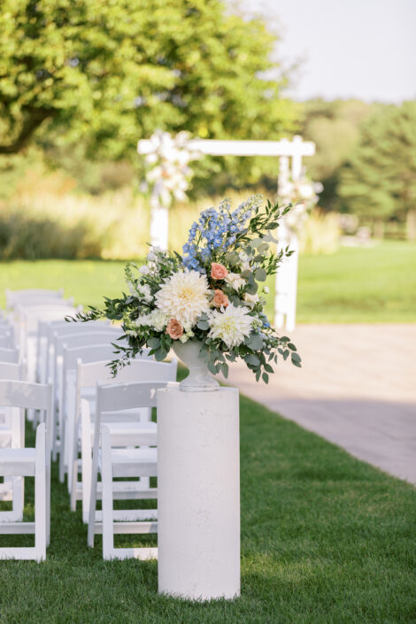 An outdoor ceremony with white chairs and flowers.