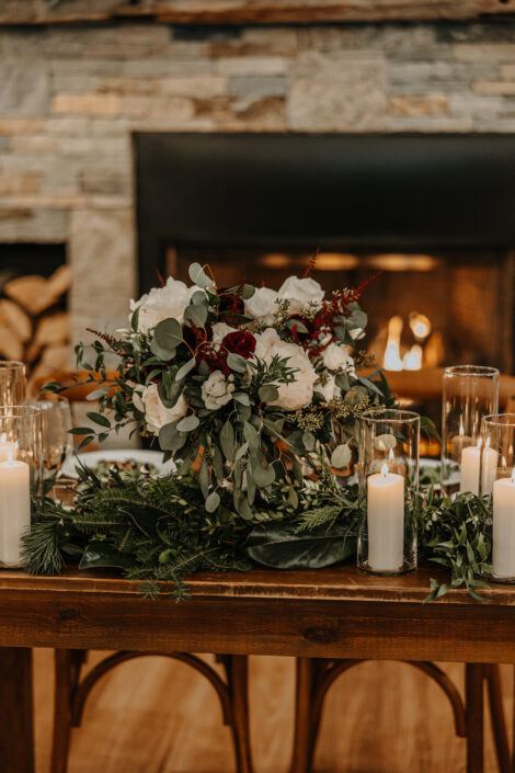 A table with candles and greenery in front of a fireplace.