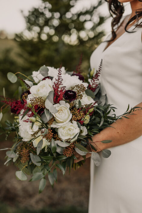 A bride in a white dress holding a bouquet of burgundy and burgundy flowers.