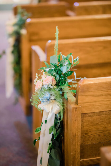 The pews at a church are decorated with flowers and greenery.