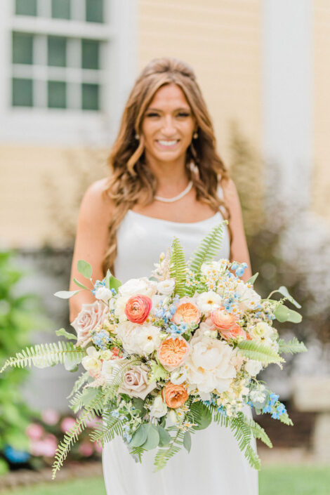A bride holding a bouquet in front of a house.